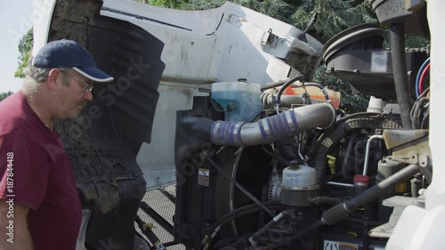 Truck driver with hood of semi truck open inspecting engine