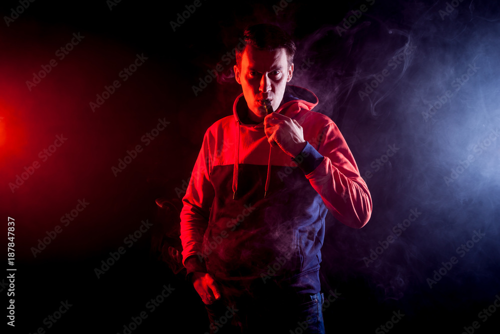 Fototapeta premium The man smoke an electronic cigarette, vape on a background of red and white smoke