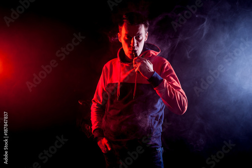 Fototapeta Naklejka Na Ścianę i Meble -  The man smoke an electronic cigarette, vape  on a background of red and white smoke