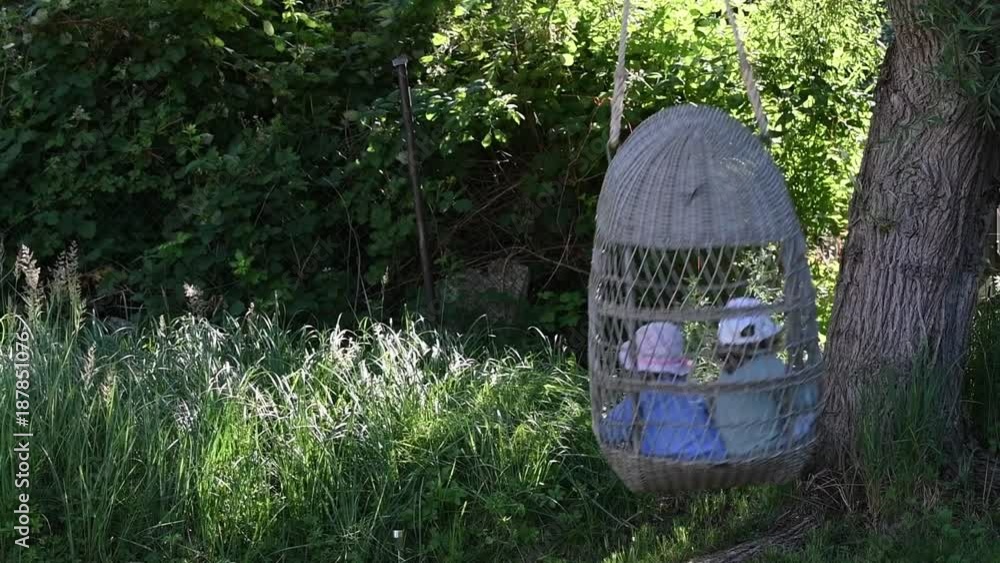 Zwei Kinder schaukeln in einer grossen Korbschaukel im Garten Stock ビデオ
