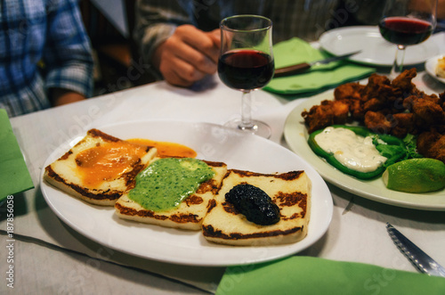 Traditional tapas plate with grilled cheese with canarian sauces mojo rojo, mojo verde and alioli, and glasses of red wine on background, Tenerife, Canary islands