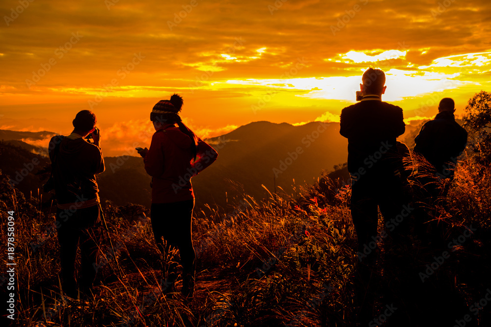 Photo silhouette and travel.They are stading on mountains and see the sunset / sunup. A man take photo and woman play mobile phone. they are fun .