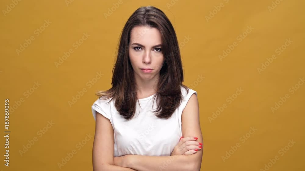 Young sad woman standing isolated over yellow background while looking camera with arms crossed. Young sad woman standing isolated over yellow background while looking camera with arms crossed.