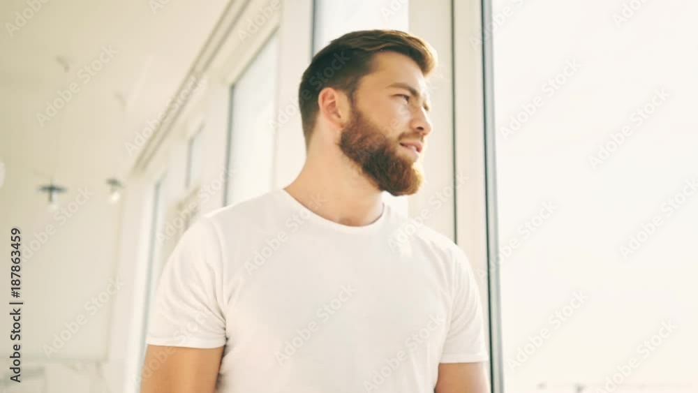 Smiling bearded man walking and looking at window indoors Smiling bearded man walking and looking at window indoors