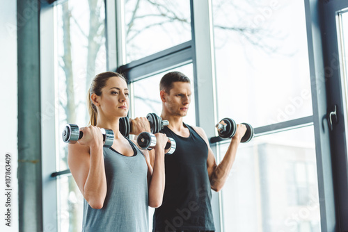 focused young man and woman exercising with dumbbells in gym