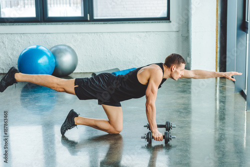 side view of young sportsman working out with dumbbells in gym