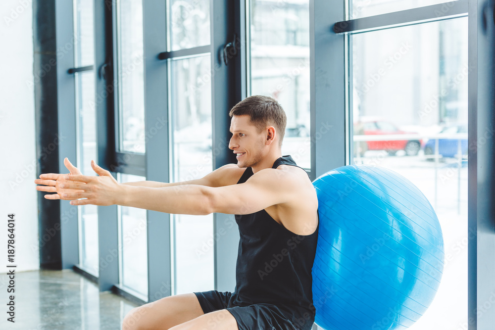 side view of smiling sportsman exercising with fitness ball in gym side view of smiling sportsman exercising with fitness ball in gym