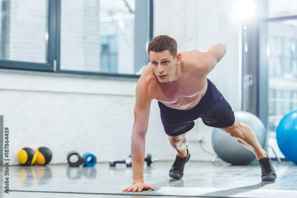 handsome shirtless young sportsman doing push ups on yoga mat