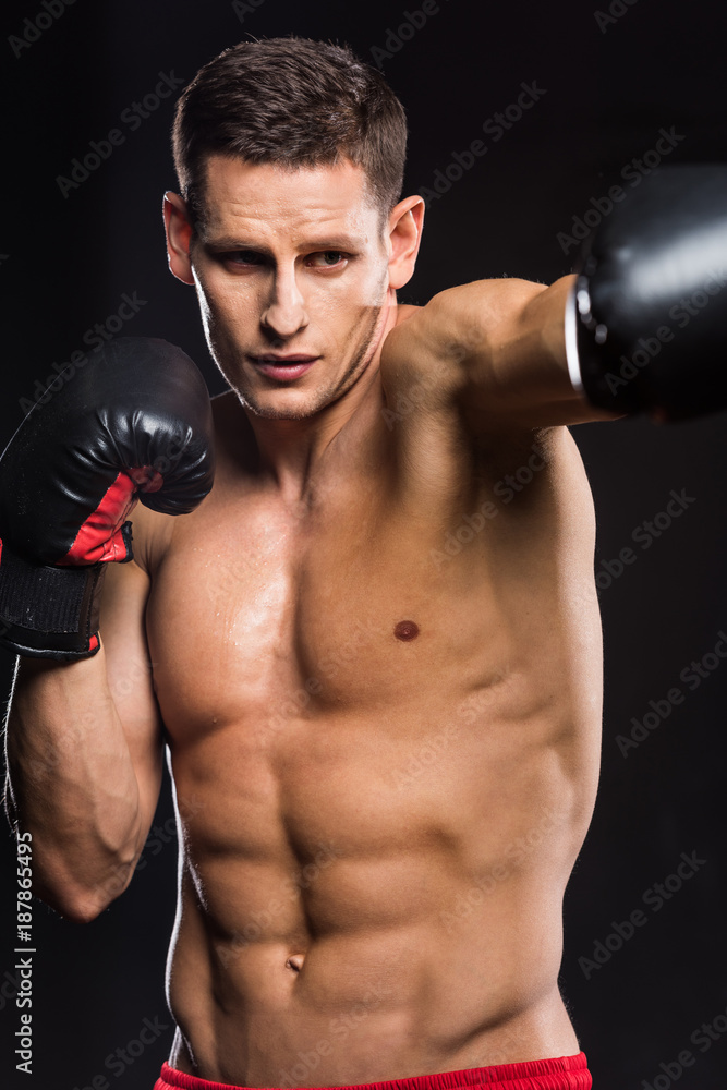 selective focus of young shirtless sportsman in boxing gloves boxing isolated on black