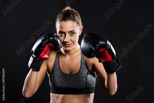 attractive young sportswoman in boxing gloves looking at camera isolated on black © LIGHTFIELD STUDIOS