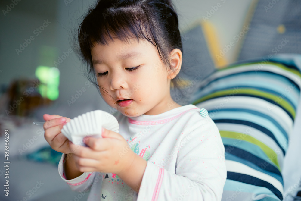 Happy Little asian girl eating brownie cake and she have spoon in her mouth in living room. Happy Little asian girl eating brownie cake and she have spoon in her mouth in living room.