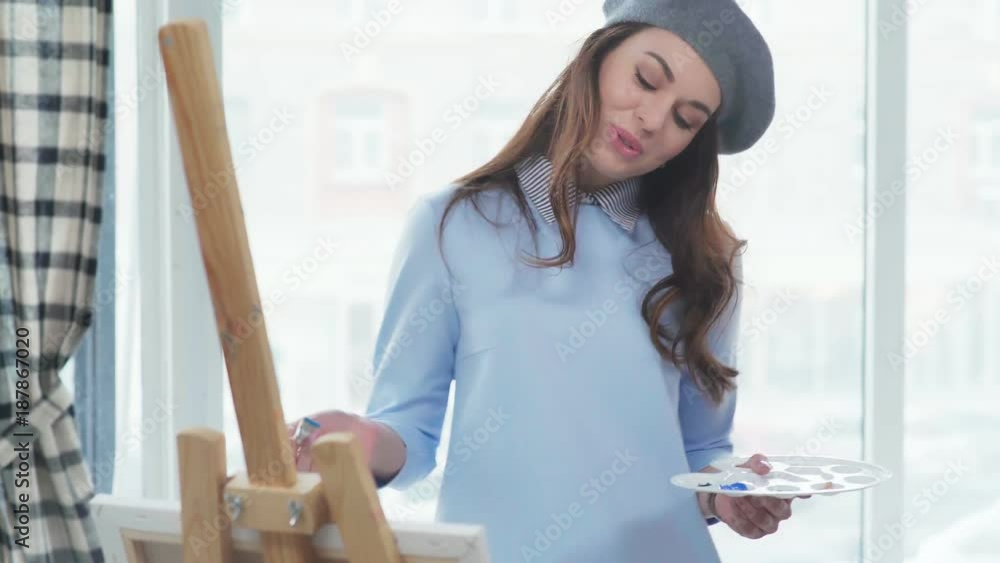 Two young beautiful women in stylish clothes are engaged in creativity and draw in a bright studio, standing at the easel. Two friends spend time together, laughing and painting. Two young beautiful women in stylish clothes are engaged in creativity and draw in a bright studio, standing at the easel. Two friends spend time together, laughing and painting.