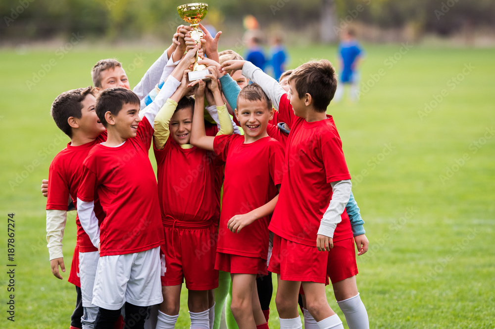 Fototapeta premium Kids soccer football - children players celebrating with a trophy after match on soccer field