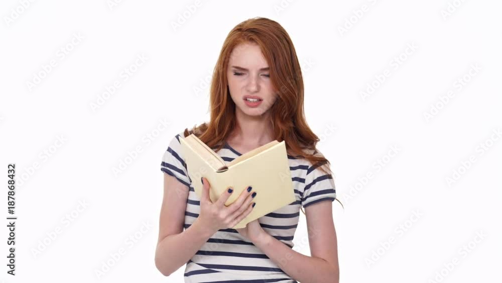 Displeased redhead young lady isolated over white wall background reading book Displeased redhead young lady isolated over white wall background reading book