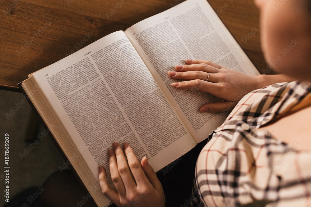 Obraz premium in the foregraund there are a large book and a girl' s plaid shirt and hands with a beautiful neat manicure.