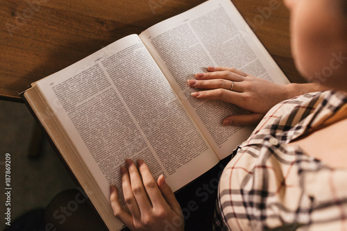in the foregraund there are a large book and a girl' s plaid shirt and hands with a beautiful neat manicure.