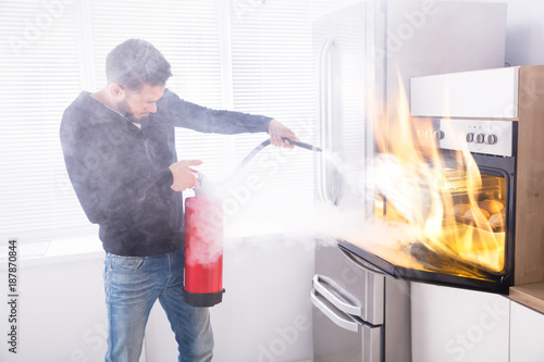 Man Using Fire Extinguisher To Stop Fire Coming From Oven photo