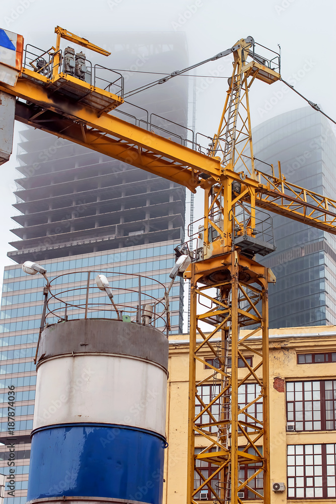 Fototapeta premium a crane at a construction site in foggy weather, on the background of the unfinished skyscrapers