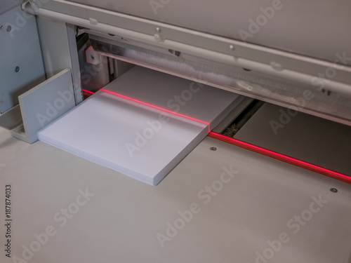 Paper cutting machine with red laser or light is cutting stack of a4 papers.