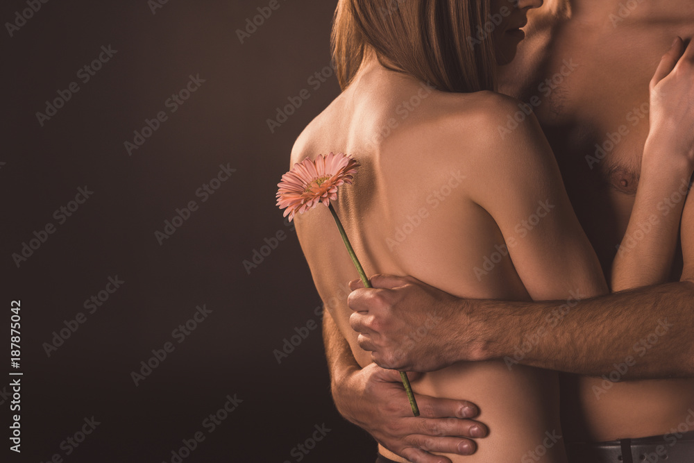 Φωτογραφία cropped view of tender couple hugging and holding flower, isolated on brown