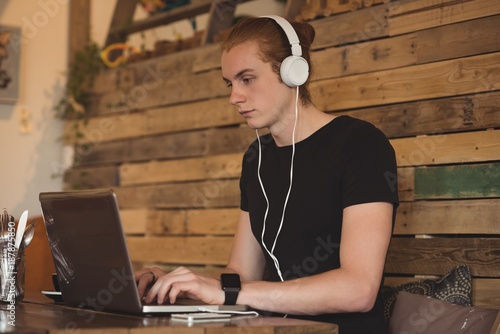 Man listening music on headphones while using laptop