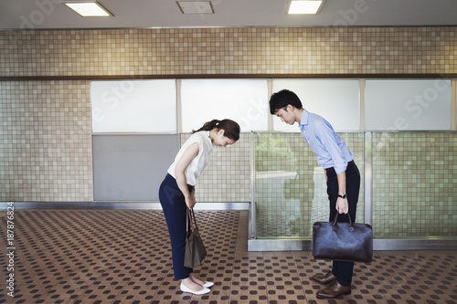 Two people greeting, a man and young woman bowing from the waist when they meet in a subway. 