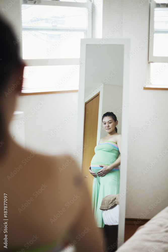 A pregnant woman standing in front of the mirror with her hands on her belly. A pregnant woman standing in front of the mirror with her hands on her belly.