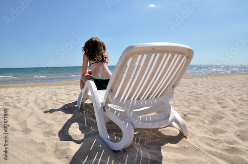 Sad young woman sitting on the lounge chair and staring at the swampy sea