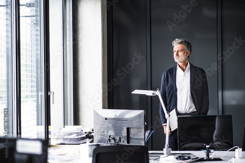 Mature businessman standing in office looking out of window