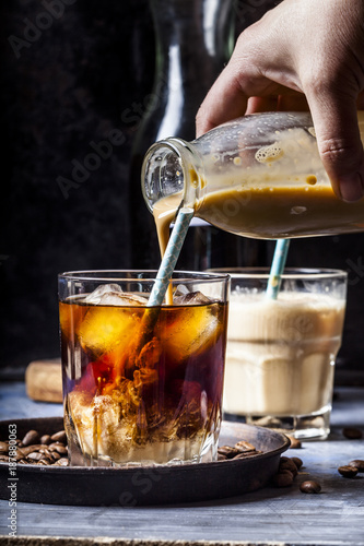 Hand pouring vanilla creamer into glass with iced coffee
