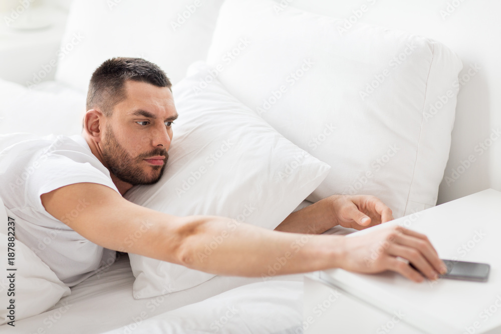 young man reaching for smartphone in bed young man reaching for smartphone in bed