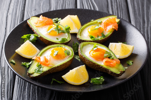 Original breakfast of avocado with egg, smoked salmon and greens close-up on a plate. horizontal