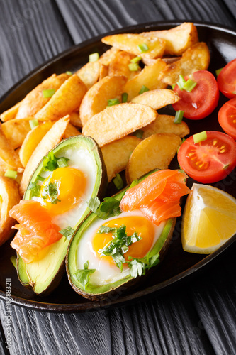 Baked avocado stuffed with eggs and salmon, fresh tomatoes and fried potato slices closeup on plate. vertical