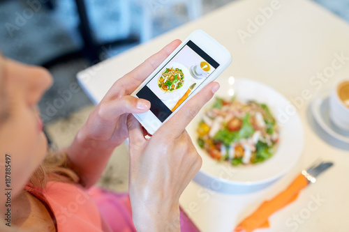 woman with smartphone photographing food at cafe