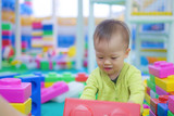 Cute little Asian 18 months / 1 year old toddler baby boy child wearing green sweater having fun playing with big colorful plastic blocks indoor