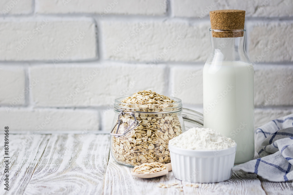 Healthy gluten free oat flakes in glass jar, milk in bottle, flour on white background. Selective focus, space for text. Healthy gluten free oat flakes in glass jar, milk in bottle, flour on white background. Selective focus, space for text.