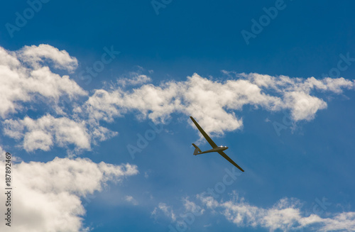 A Glider flying in bleu sky with big white clouds. The glider is a plane that has no engine
