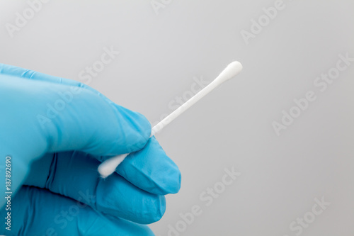 Hand in blue glove holding tweezers with a cotton bud