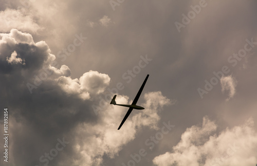 A Glider flying in sky with big threatening clouds. The glider is a plane that has no engine