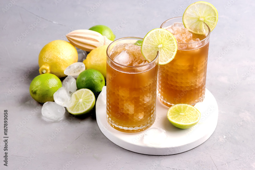Glass of Tsasty Ice Tea with Ice Cubes and Citrus Cold Summ er Beverage Wooden Squeezer and Raw Lemons and Limes on Background Above Glass of Tsasty Ice Tea with Ice Cubes and Citrus Cold Summ er Beverage Wooden Squeezer and Raw Lemons and Limes on Background Above
