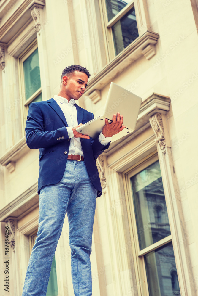 Way to Success. African American college student studies in New York. Wearing blue blazer, white shirt, man stands outside vintage office building, works on laptop computer. Filtered effect.