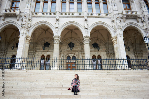 Sweet girl sitting on the steps of the Palace of Parliament in Budapest, Hungary. Autumn