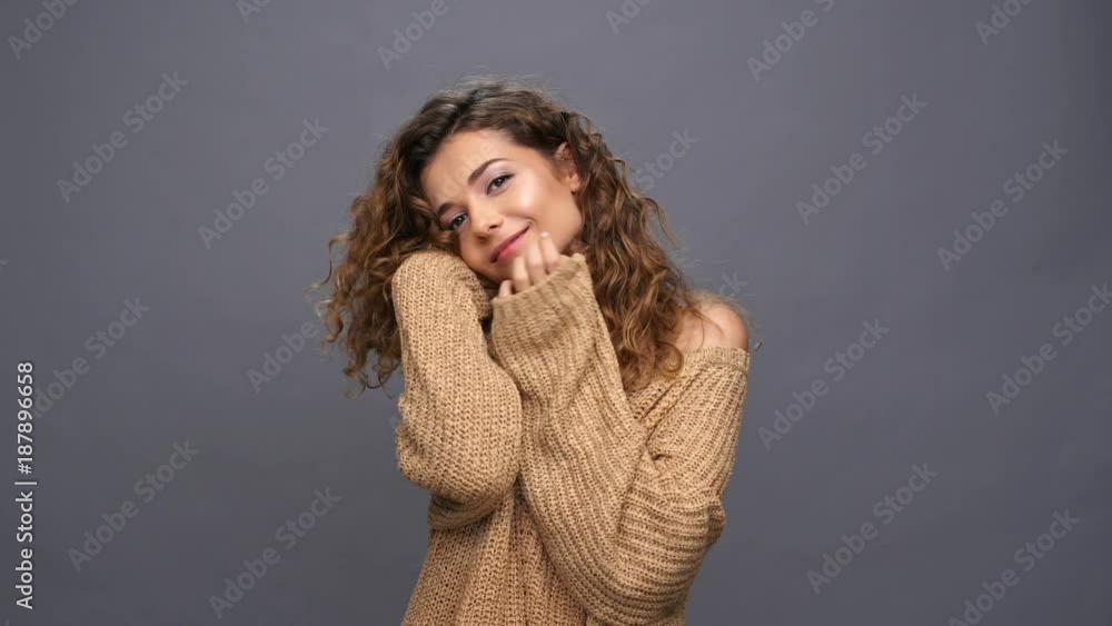 Pleased beauty curly woman in sweater warmed and touching her face over purple background Pleased beauty curly woman in sweater warmed and touching her face over purple background