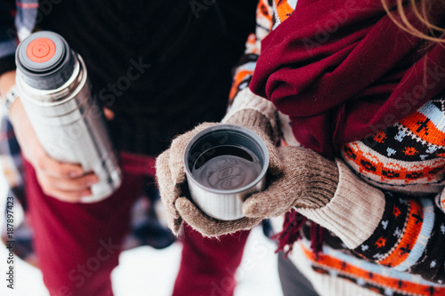 woman hands pours hot tea or coffee out of thermos on winter forest background. girl using a thermos in on a snowy day. metallic cup