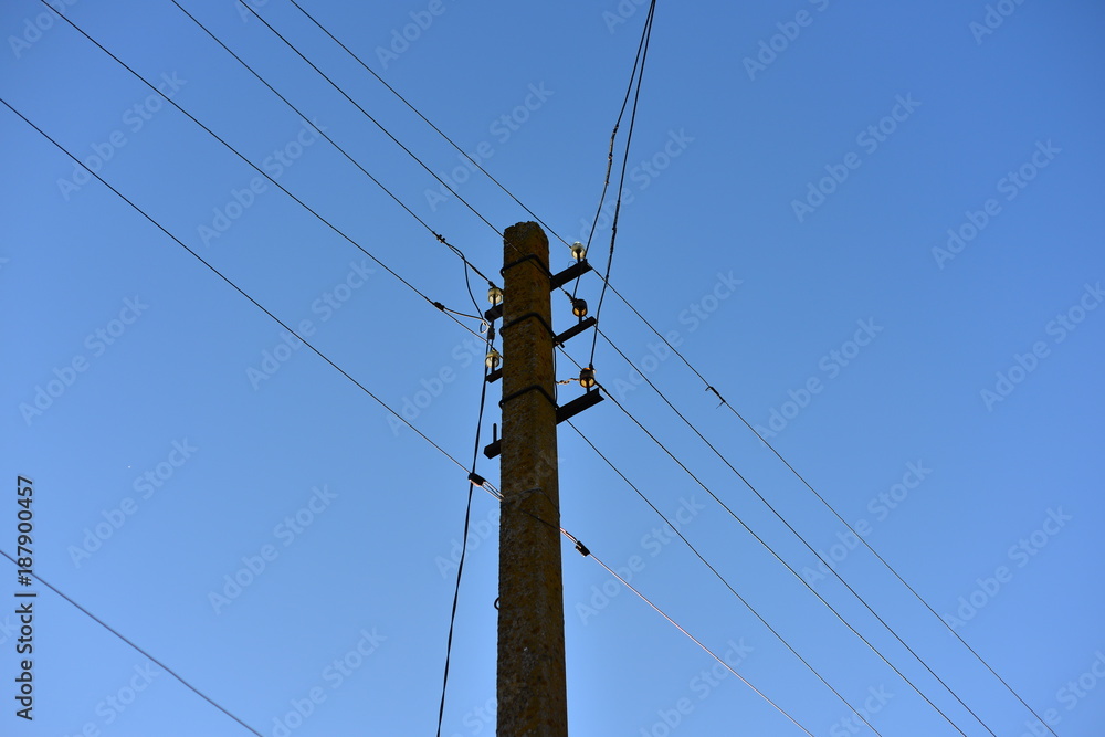 Utility Pole against Blue Sky supporting overhead power lines, electrical cable, fibre optic cable, transformers and street lights.