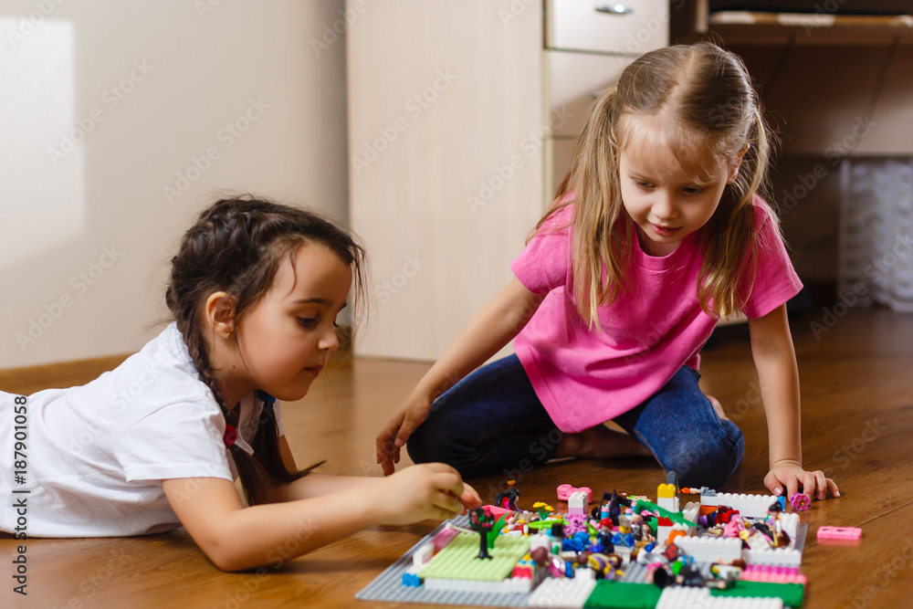Fototapeta premium Two cute little children are playing with blocks happy girls at home funny lovely sisters