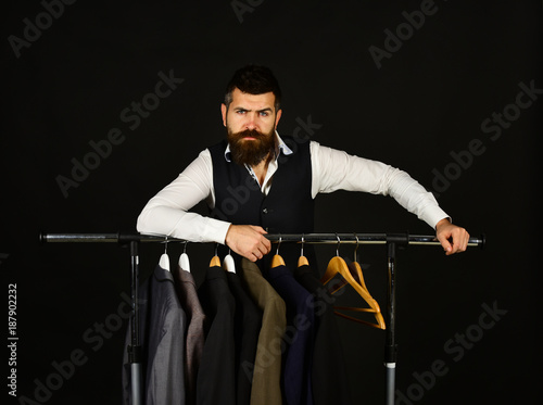 Man with beard in vest by clothes rack.