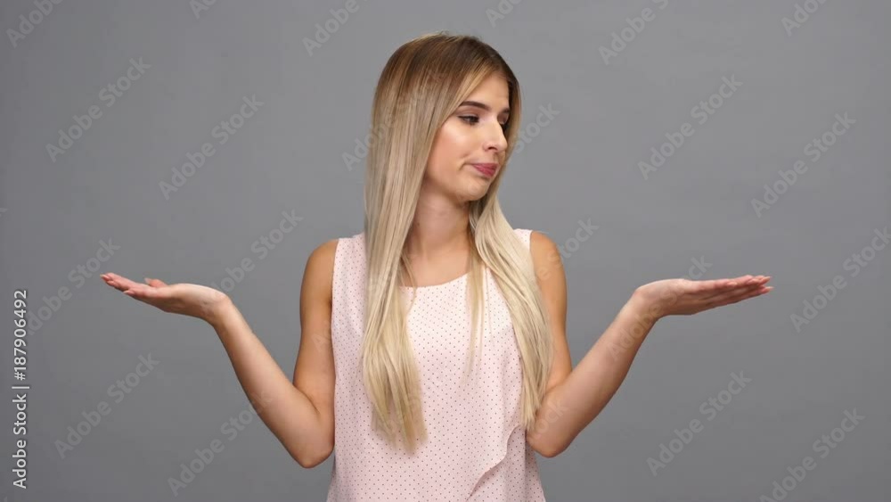 Pensive blonde woman holding copyspace on the palms and choosing something over gray background Pensive blonde woman holding copyspace on the palms and choosing something over gray background