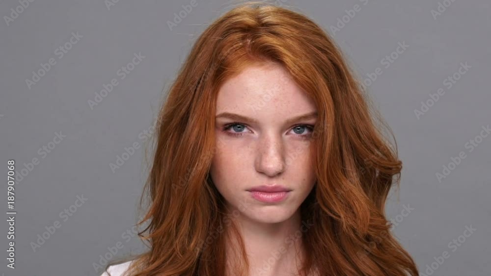 Close up view of smiling ginger woman in t-shirt looking at the camera over gray background Close up view of smiling ginger woman in t-shirt looking at the camera over gray background