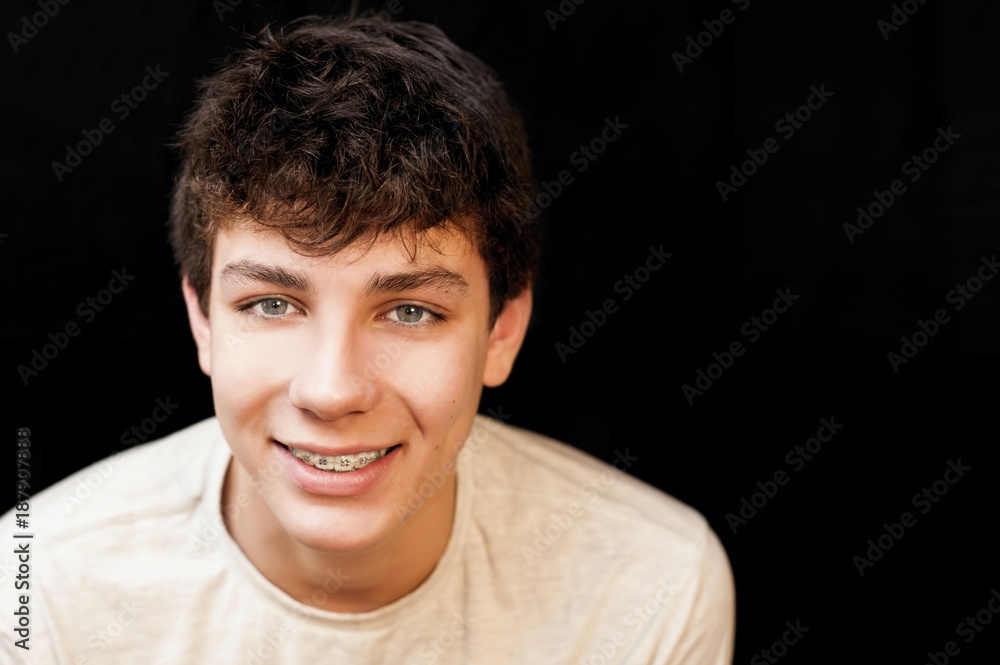 Fototapeta premium A guy with braces on his teeth in a white T-shirt on a black background